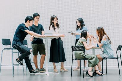 Six students sit and stand around classroom desks.