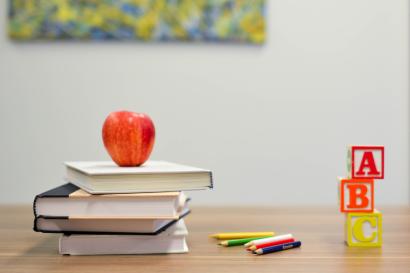 A pile of books with a red apple sitting on top. Next to the stack are ABC blocks stacked.