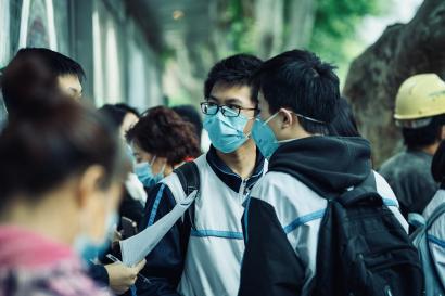 Students with backpacks in a crowd outdoors wearing face masks.