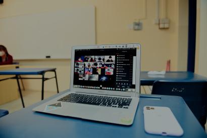 Laptop with virtual meeting on a desk in a classroom.