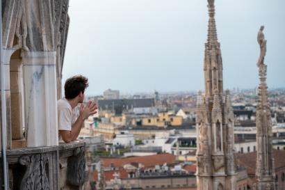 A student leaning casually out of a tower in the Duomo is overlooking the city of Milan stretching away to the horizon