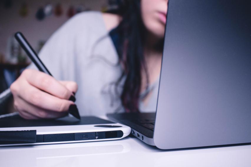 Student working on laptop and writing.