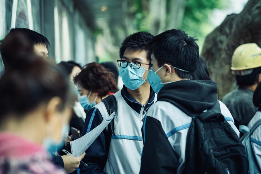 Students with backpacks in a crowd outdoors wearing face masks.