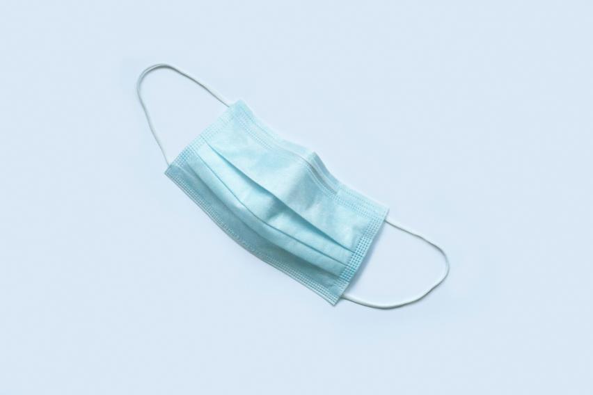 Photo of a blue-green disposable face mask on a light blue background
