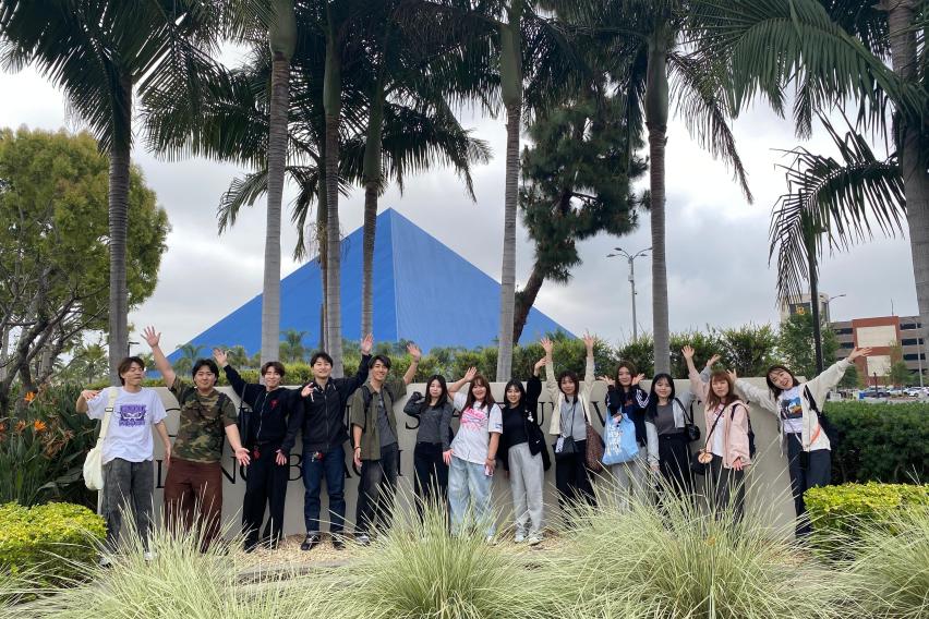 Group of students on the CSULB campus with palm trees and the Walter Pyramid Stadium in the background.