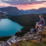 a man sits on a rock overlooking a lake at sunset