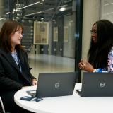 student intern sitting at desk with manager and two open laptops