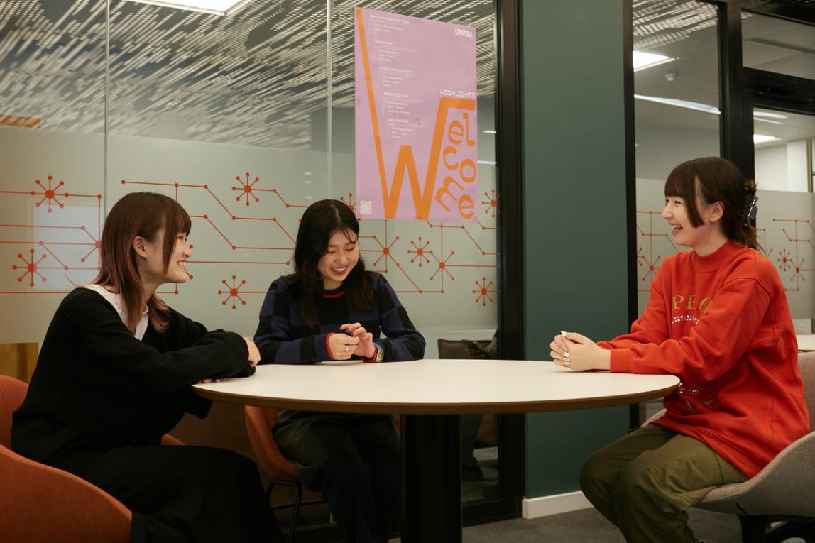 Three female SAF students engaged in conversation at a table inside the University of Westminster.