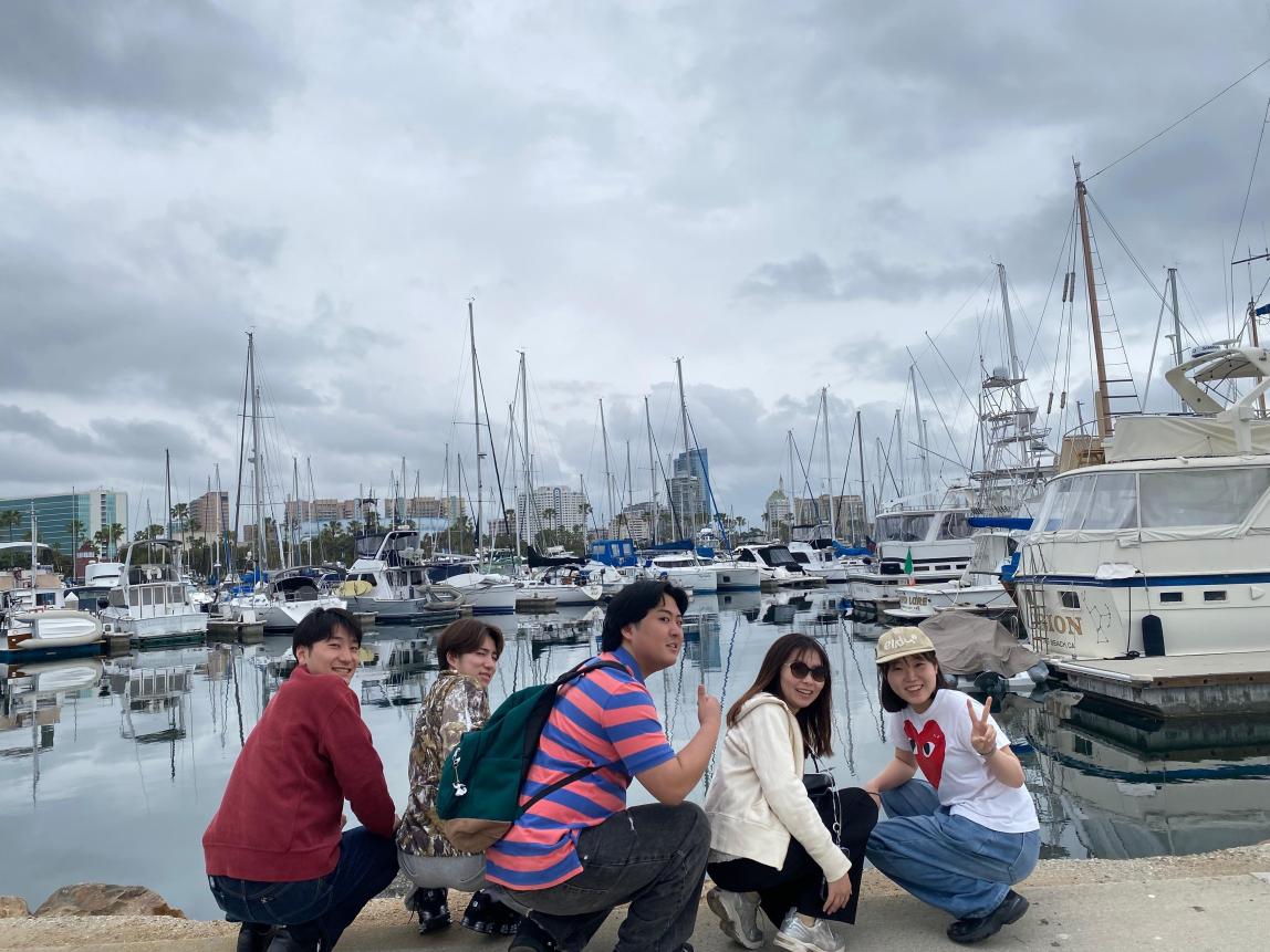 Five students crouched at a boat dock.