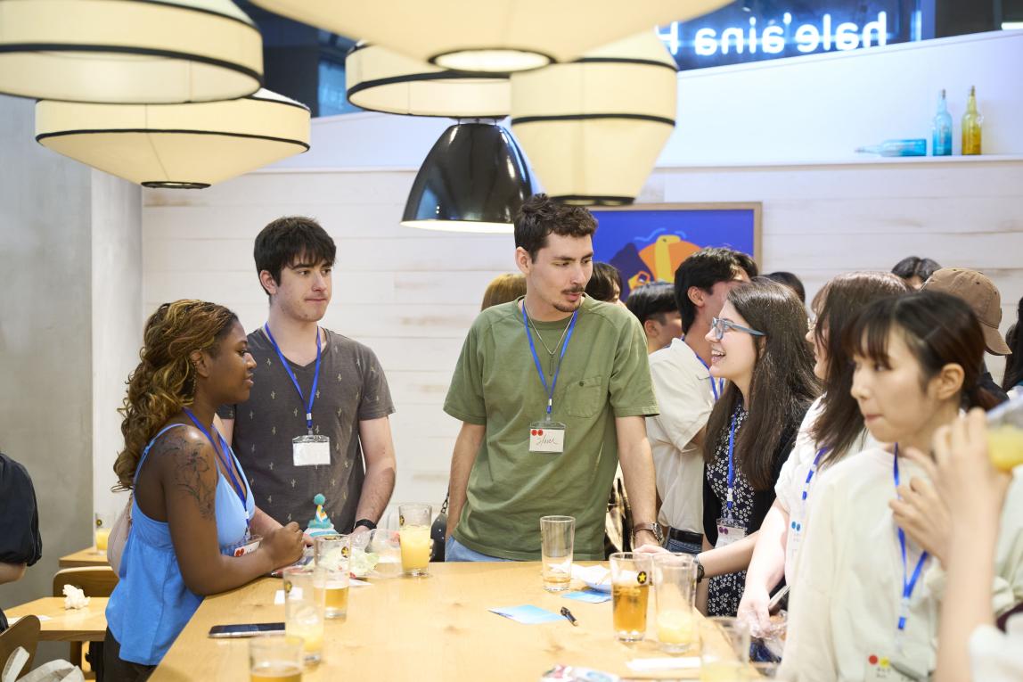 Group of students conversing, standing around a table.
