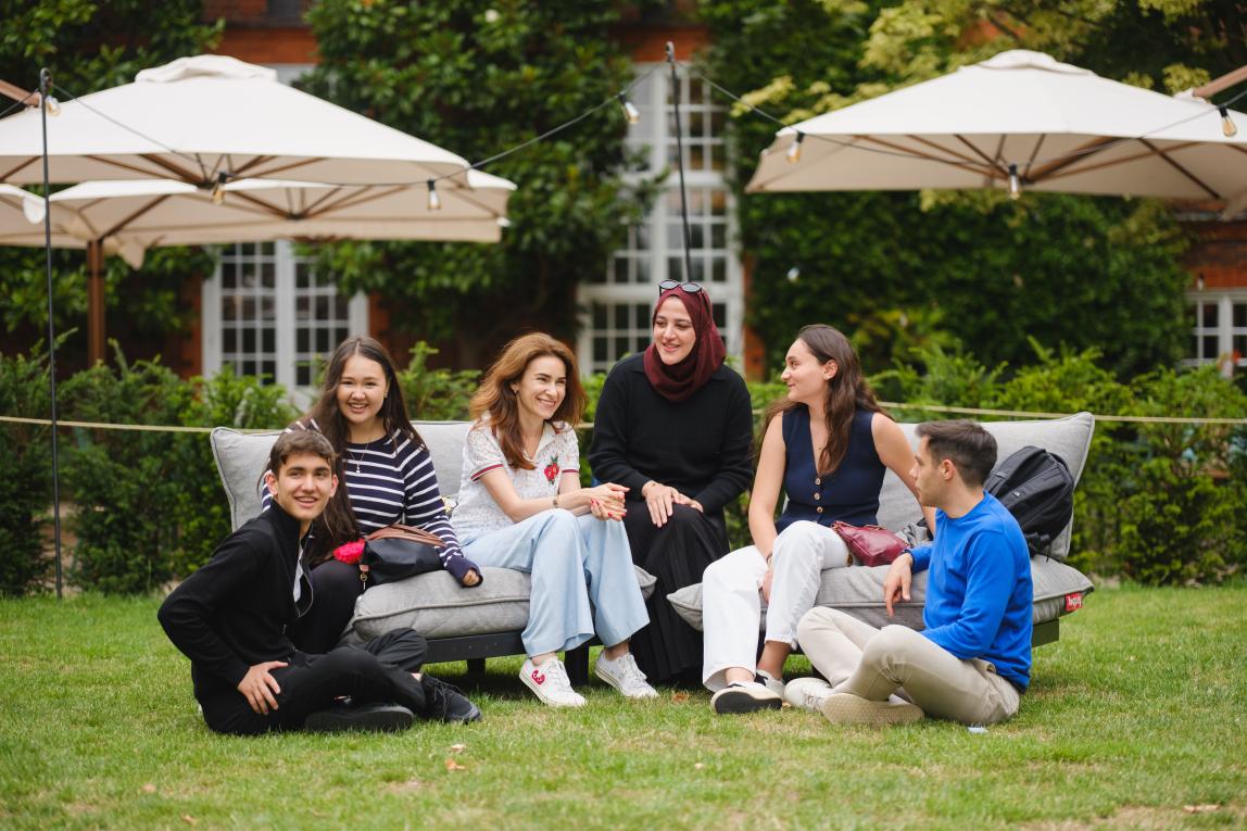 Group of students sitting in Regent's University London courtyard, patio umbrellas behind them. 