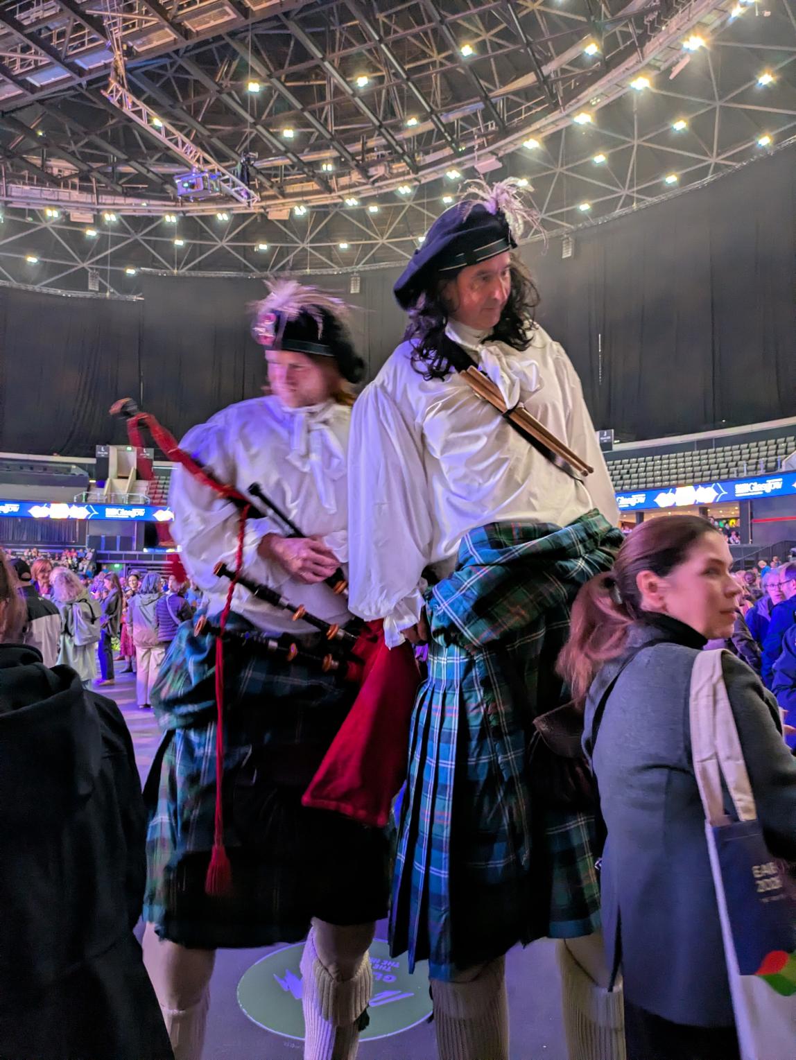 Two people dressed in traditional Scottish attire walking on stilts. 