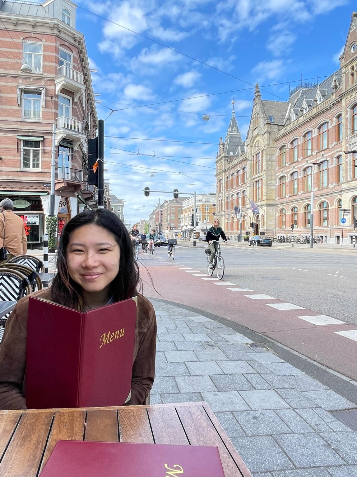 a student sitting on an outdoor restaurant patio with a menu in Amsterdam