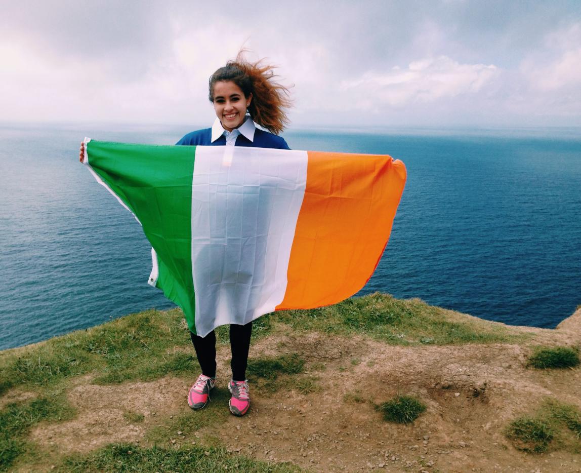 a student holding an Irish flag at the Cliffs of Moher