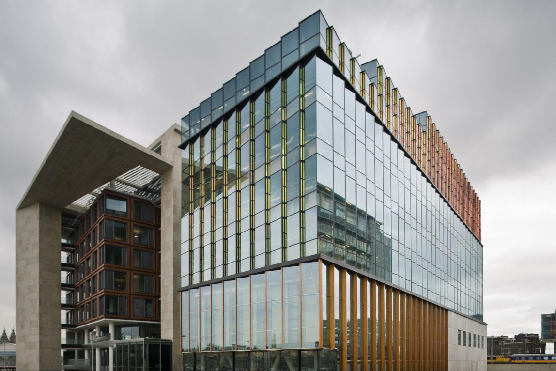 A large, modern building sits on the Conservatorium van Amsterdam's campus with reflective windows.