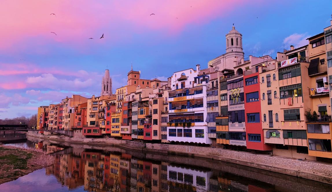 multicolored buildings bordering a lake with pink clouds and a blue sky