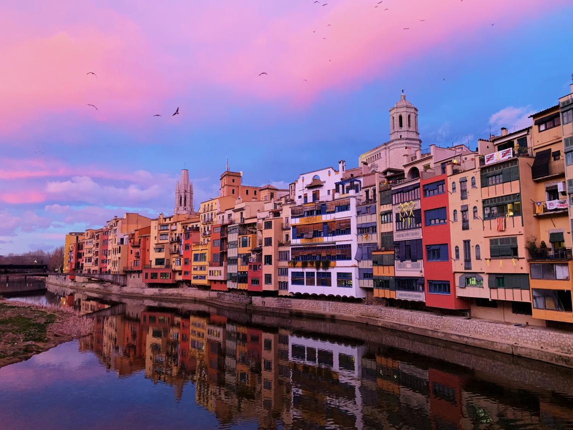 multicolored buildings bordering a lake with pink clouds and a blue sky