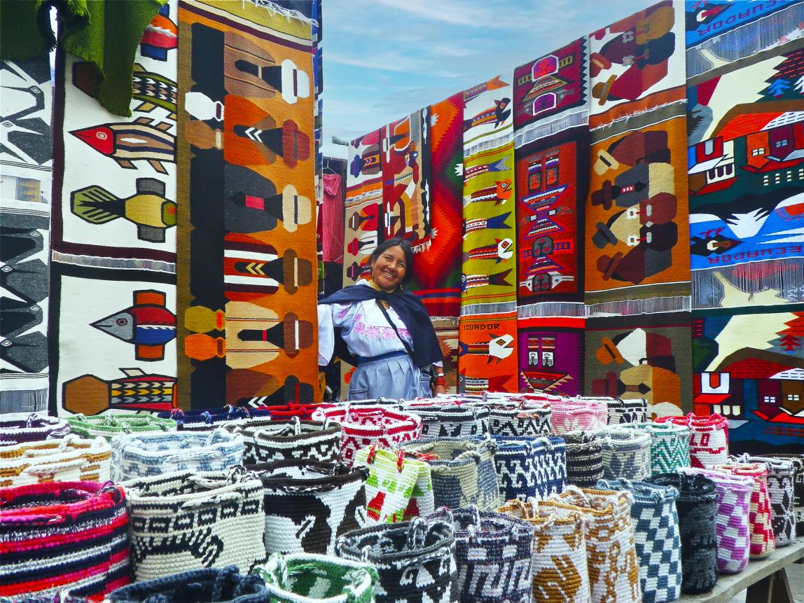 a seller at the market in Otavalo surrounded by colorful quilts