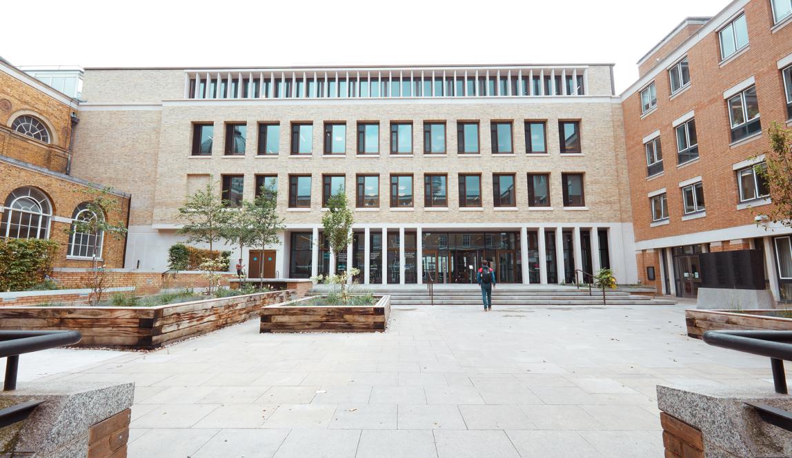 A student enters University College London, a brick building with multiple windows.
