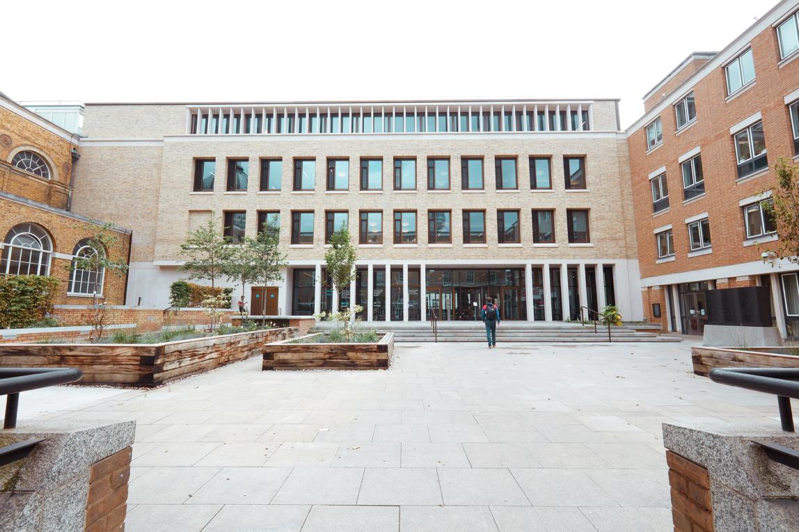 A student enters University College London, a brick building with multiple windows.