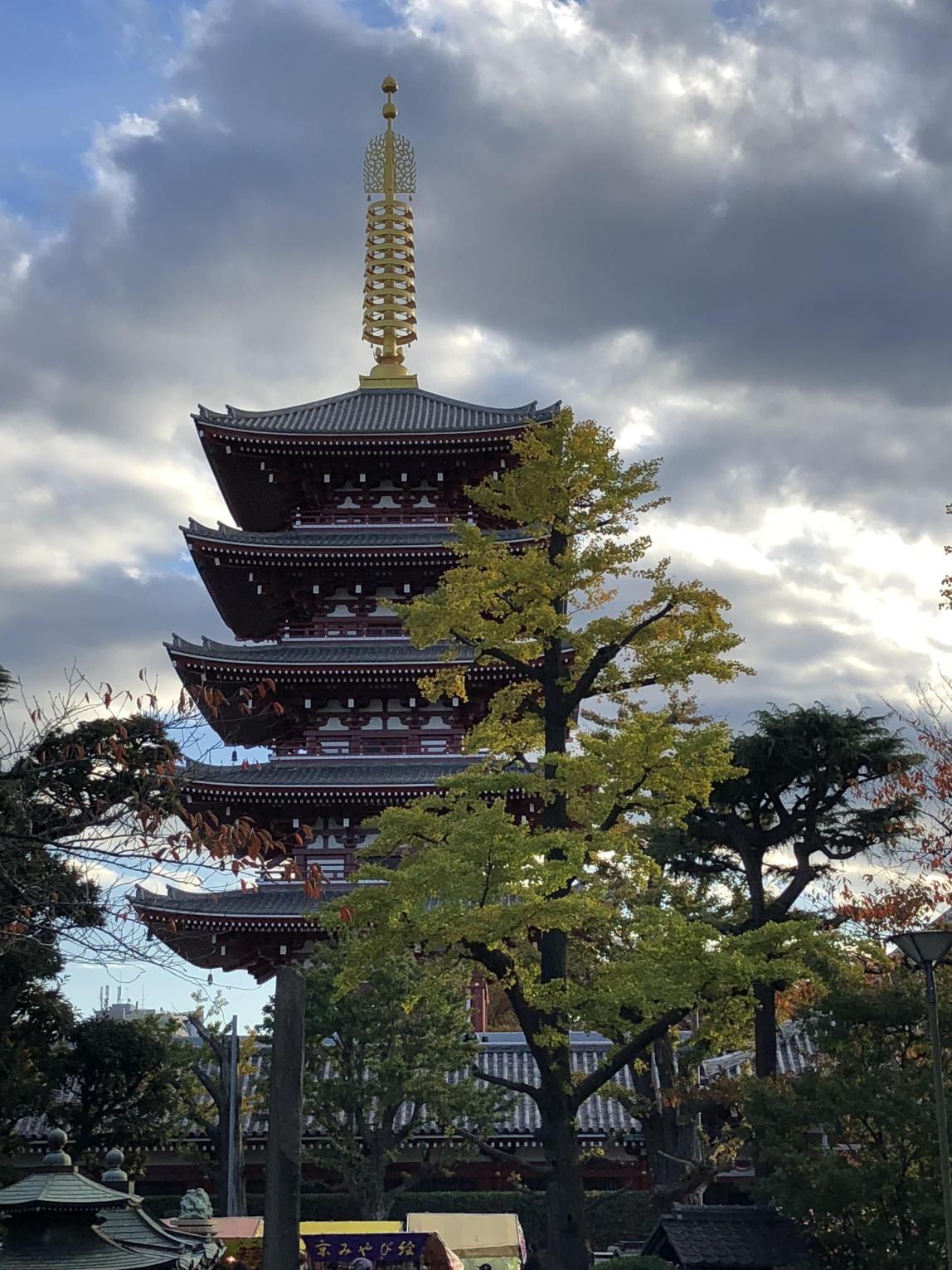 The Sensoji tower with trees and clouds framing it. The tower has a large golden spire at the top.