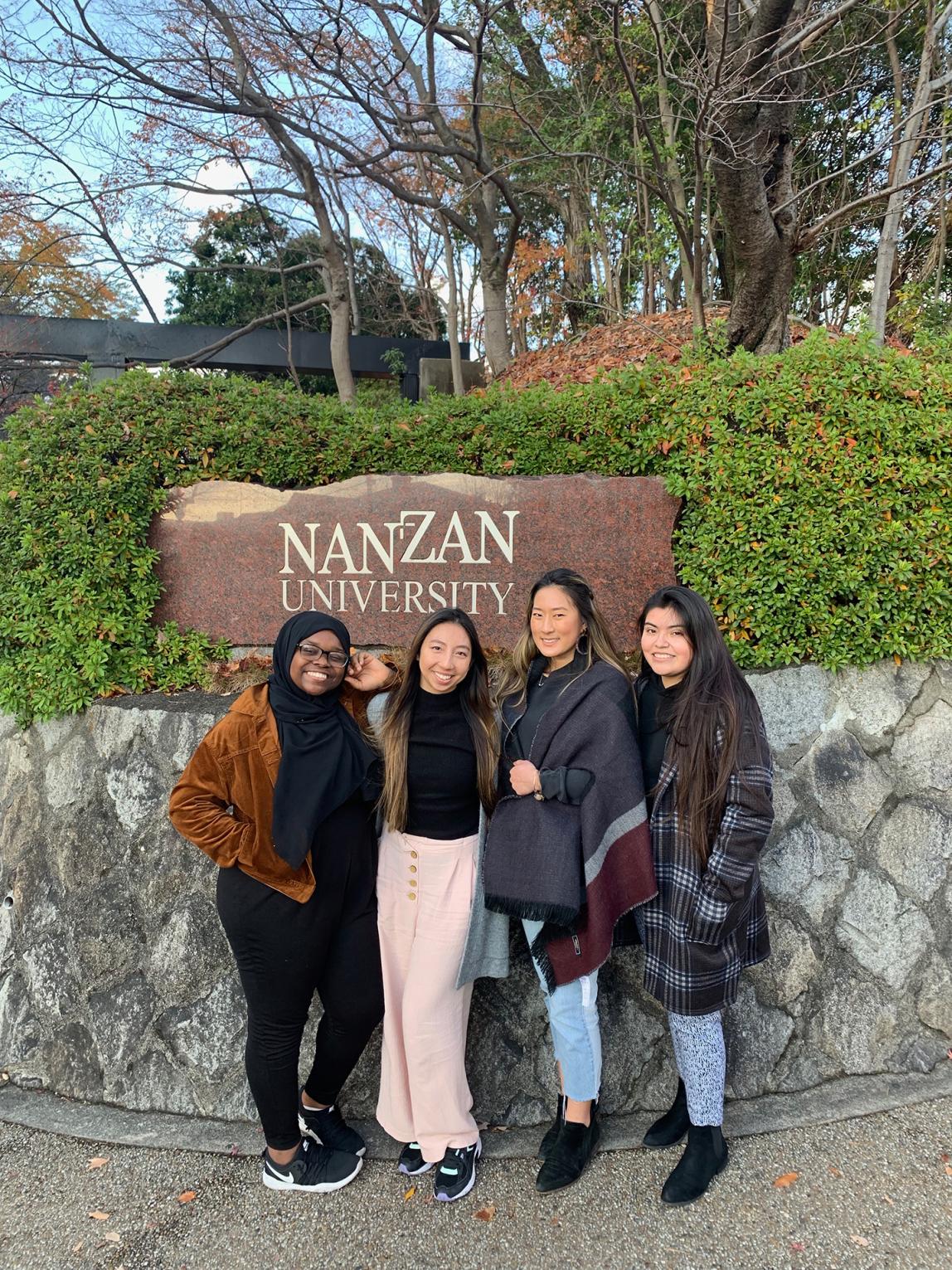 Students pose outside of Nanzan University's sign. The text reads: "Nanzan University."