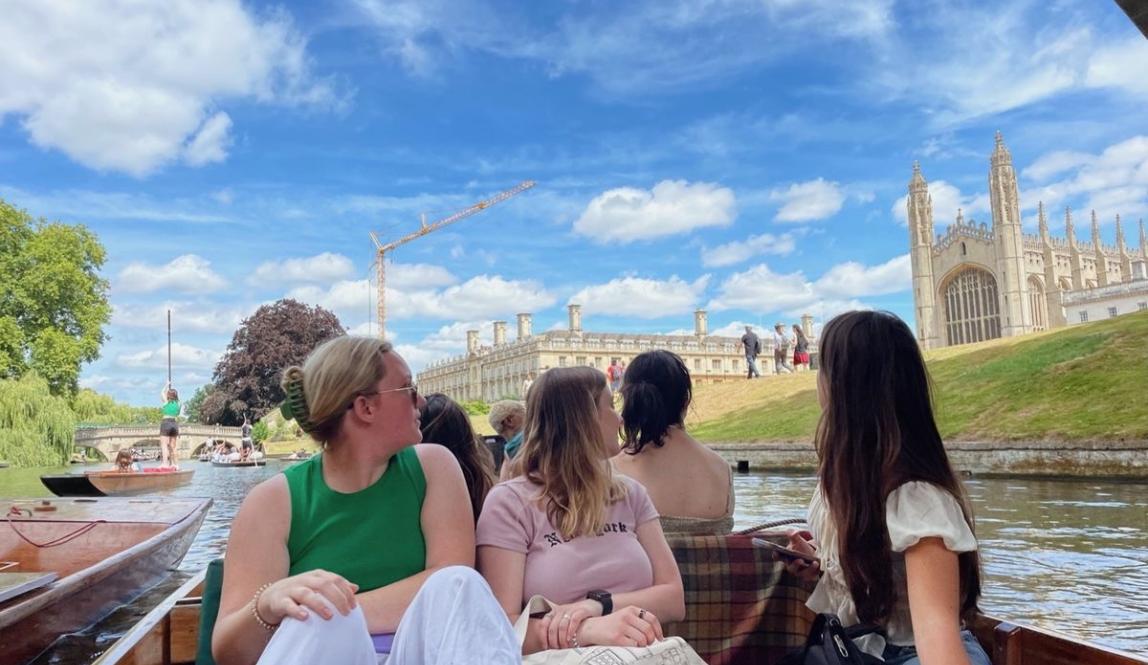 students sitting in a boat in Cambridge, looking behind them at the architecture