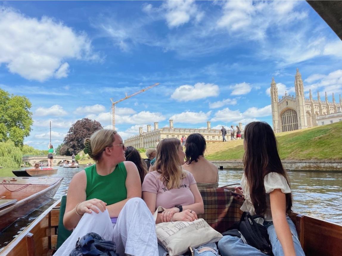 students sitting in a boat in Cambridge, looking behind them at the architecture