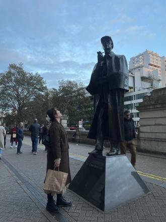 A student poses with a bronze statue of Sherlock Holmes in London
