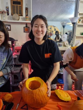 A student poses with a pumpkin she is carving