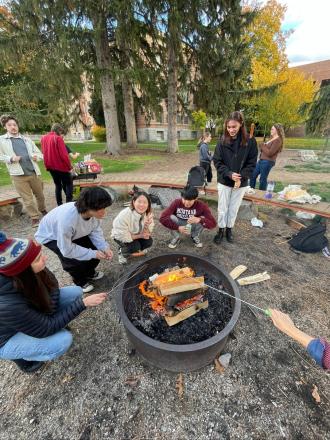 A group of University of Montana students roast marshmallows over a fire pit