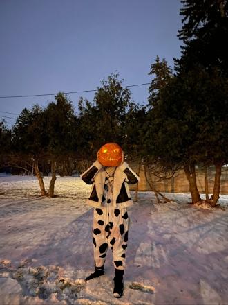 A student poses in the snow holding a jack-o-lantern in front of their face