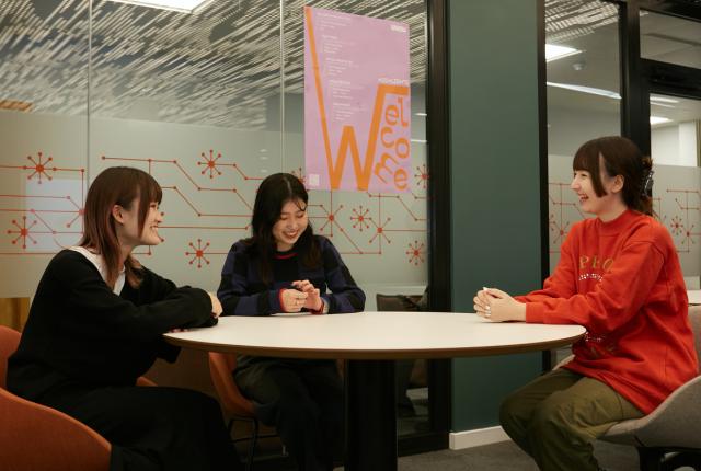 Three female SAF students engaged in conversation at a table inside the University of Westminster.