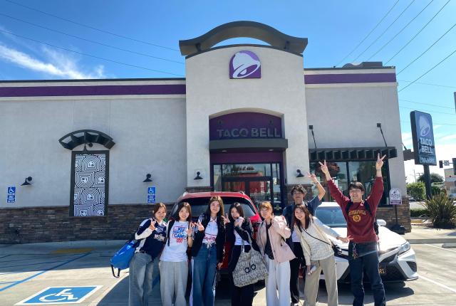 Group of students excited in a Taco Bell parking lot.