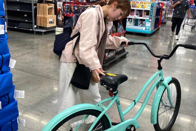 Female student inspecting a blue cruiser bicycle inside of Walmart.