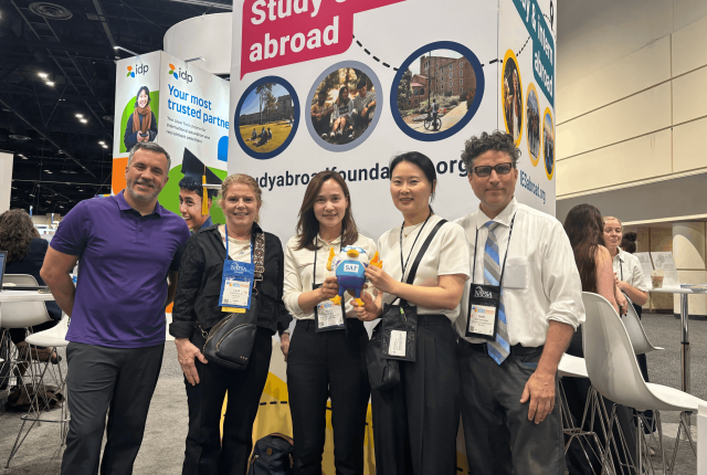 SAF Leadership pose in front of the IES Global booth with a university partner and SAFFY doll at NAFSA 2026.