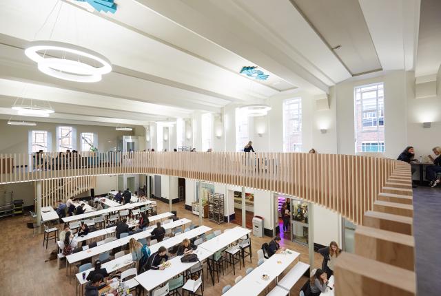 Wide shot of cafeteria in Regent's University London, students at tables conversing and eating. 