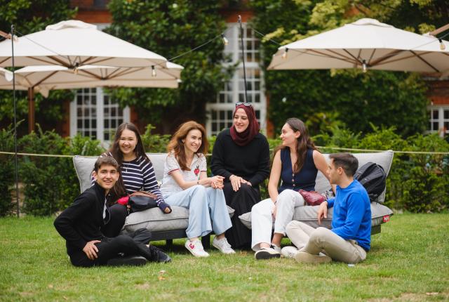 Group of students sitting in Regent's University London courtyard, patio umbrellas behind them. 