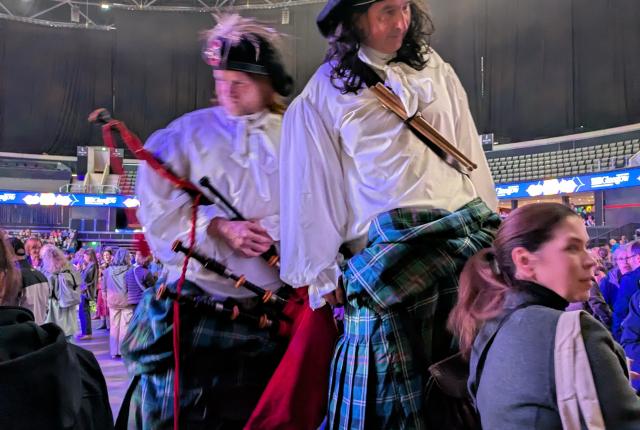 Two people dressed in traditional Scottish attire walking on stilts. 