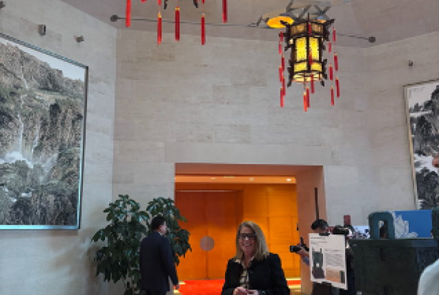 Carol Carmody at the 77th Anniversary PRC event entrance, standing under two ornate Chinese lanterns.