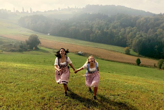 students running up a hill in dirndl dresses on the boarder of Austria
