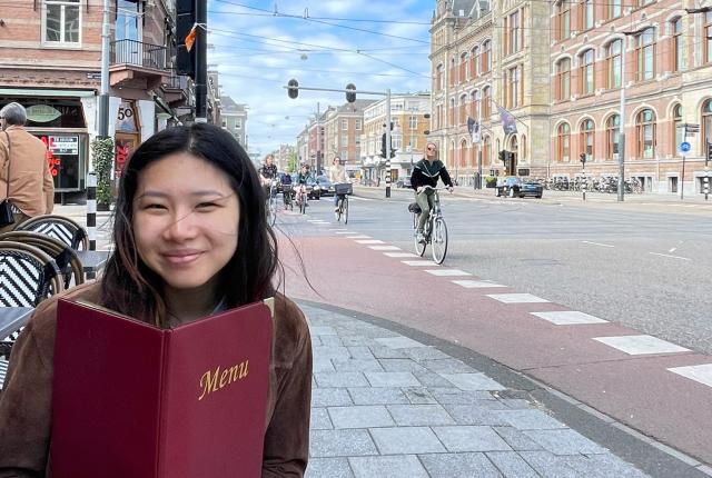 a student sitting on an outdoor restaurant patio with a menu in Amsterdam