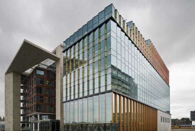 A large, modern building sits on the Conservatorium van Amsterdam's campus with reflective windows.