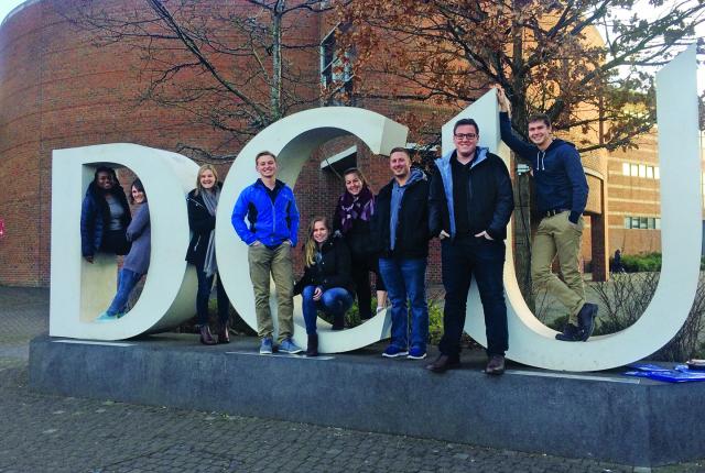 Students stand on Dublin City University's giant letter display. The letters are "DCU."