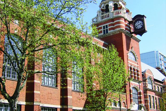 Students walk outside the University of London, a brick building with a round spire.