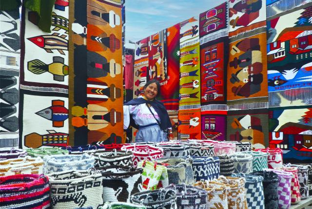 a seller at the market in Otavalo surrounded by colorful quilts