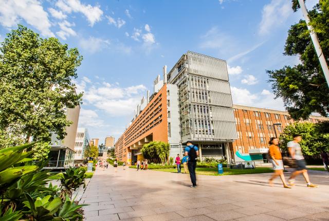 Students make their way to class on UNSW's campus, with tall brick buildings along the main walkway.