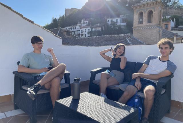 Three students sitting on the patio of the Granada Center with the sun shining behind them