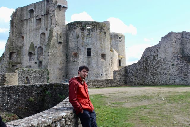 A student poses in front of ruins of an old, stone building on a sunny day.