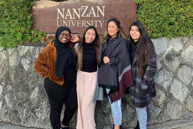 Students pose outside of Nanzan University's sign. The text reads: "Nanzan University."